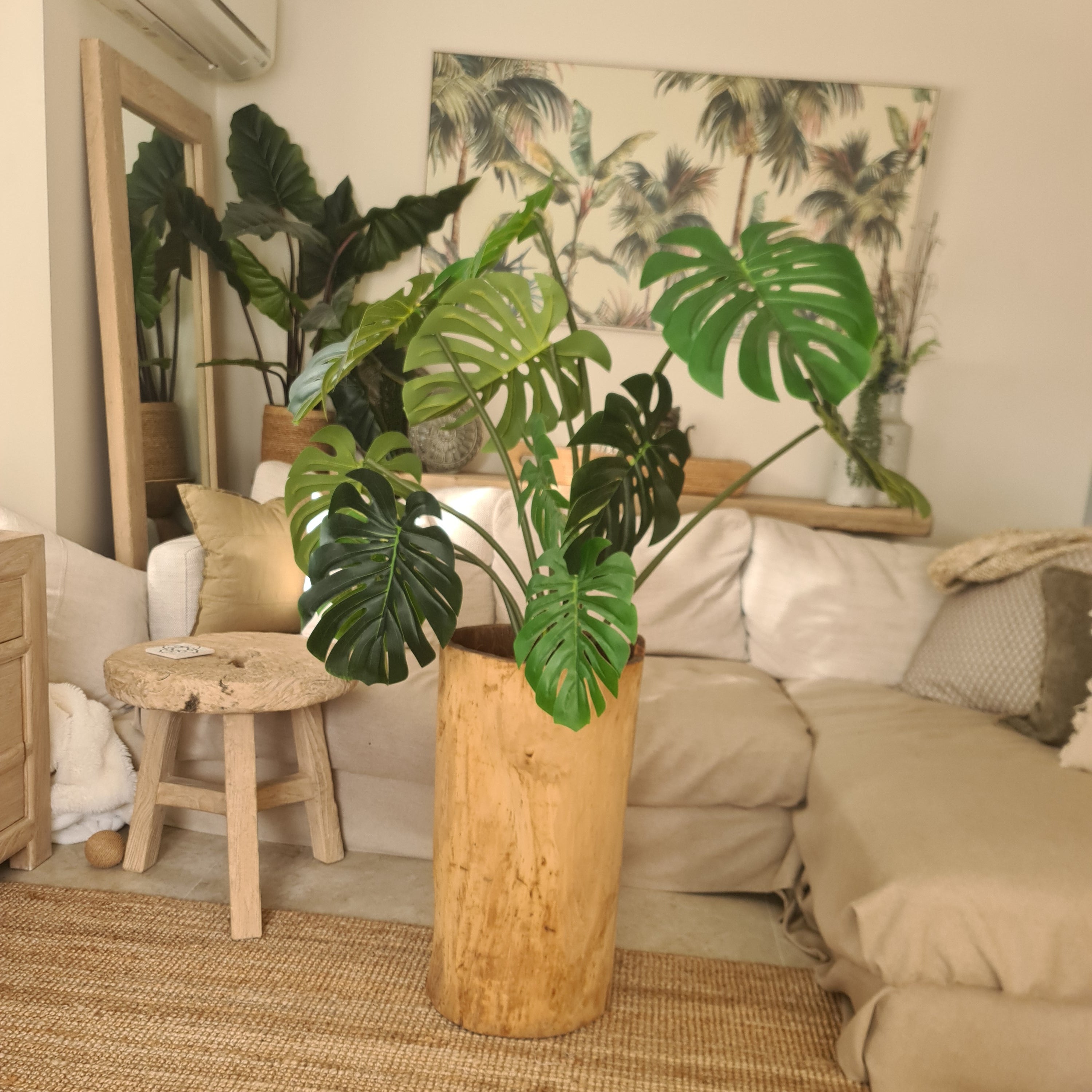 Living room with a plant on a wooden stool, sofa, and wall art.