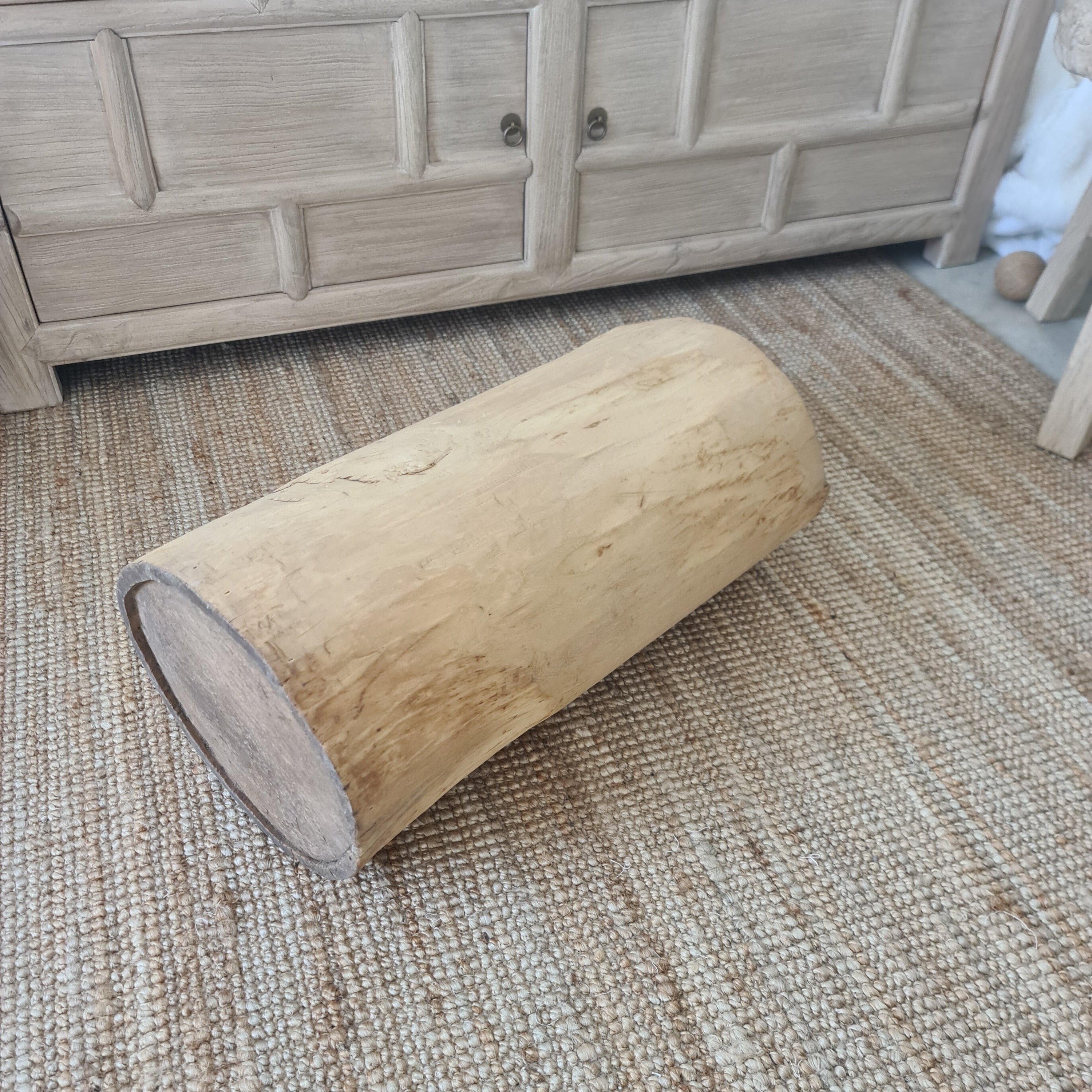 Wooden cylindrical object on a textured surface next to wooden furniture.